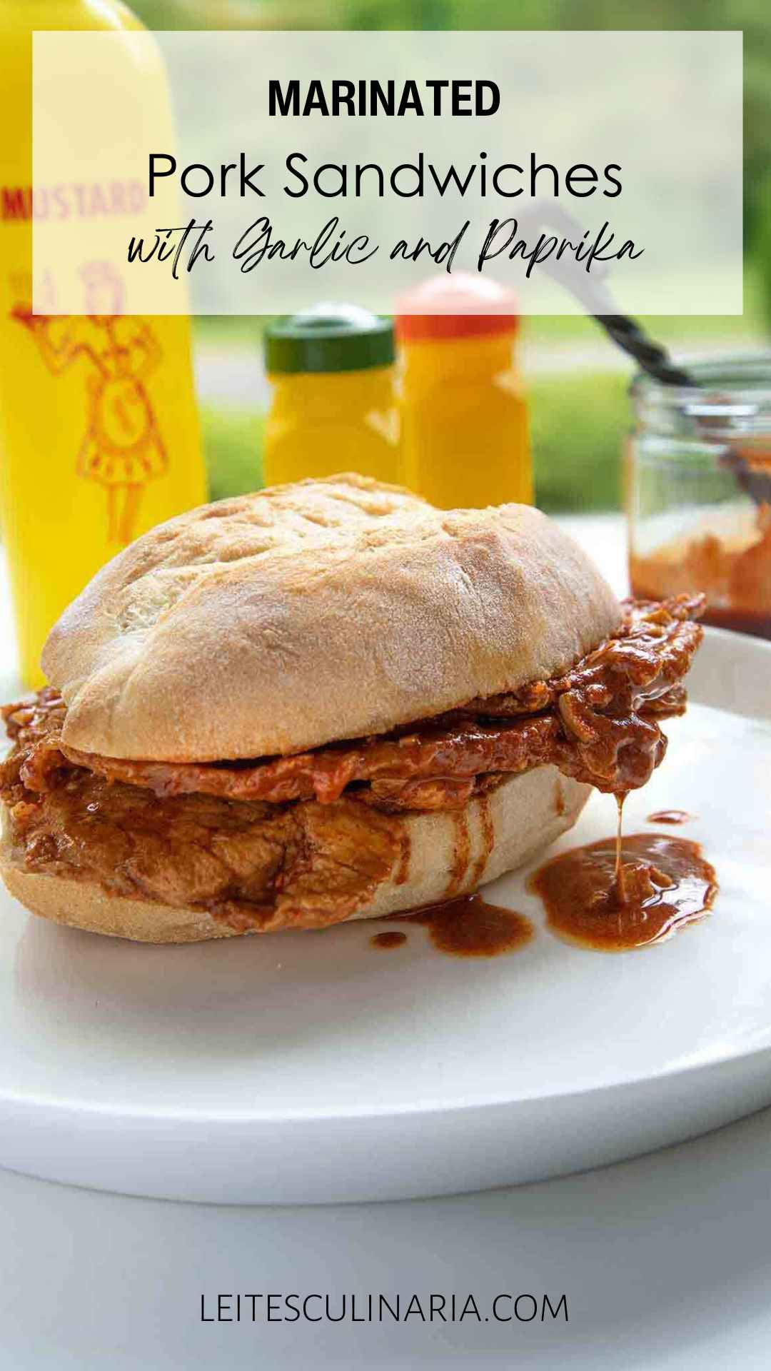 A sandwich made with a large roll, thinly sliced pork, and a paprika sauce dripping out of it on a white plate.