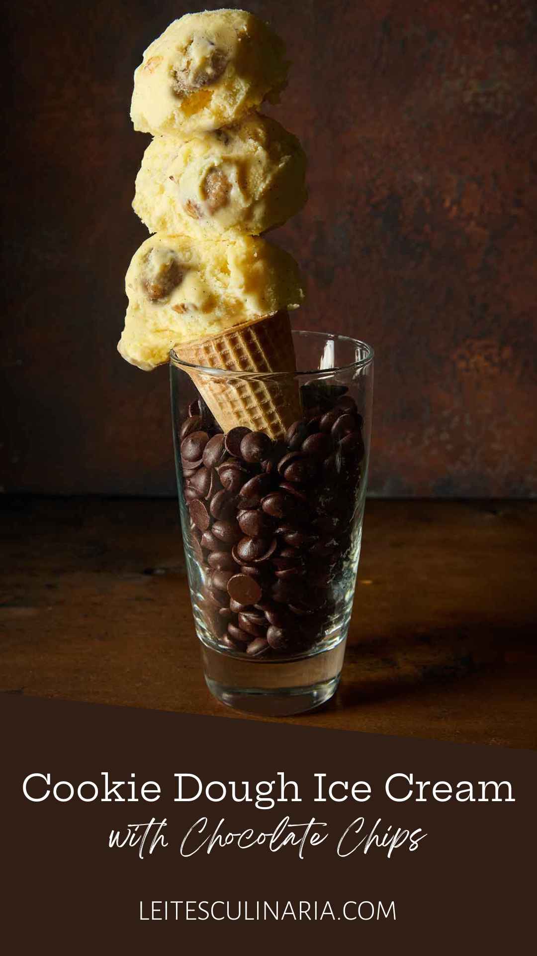 A sugar cone of chocolate chip cookie dough ice cream in a tall glass of chocolate chips.