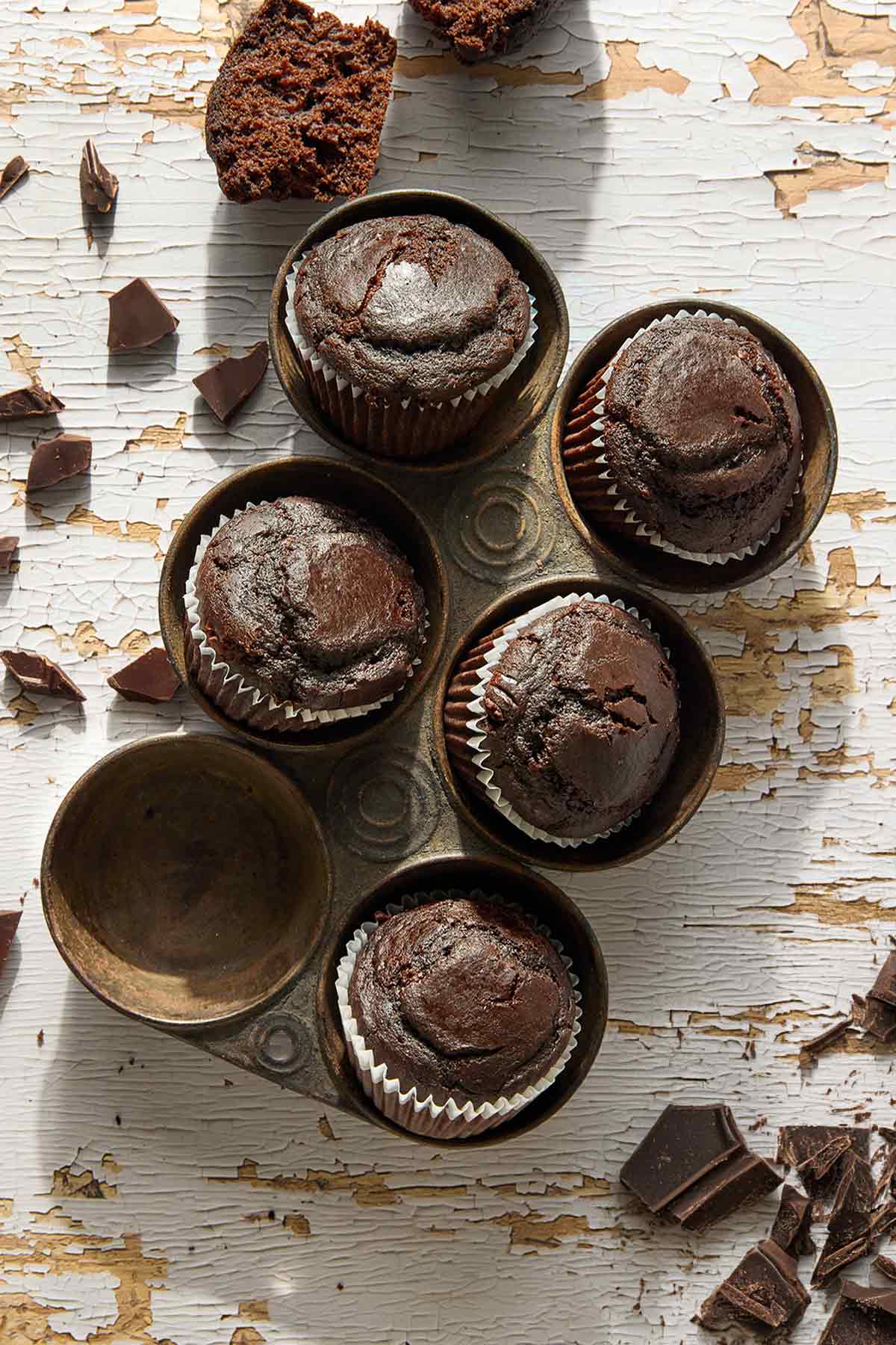 Five chocolate muffins in an antique muffin tin.
