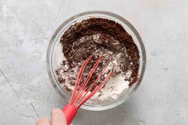 A person whisking flour, cocoa, and sugar together in a bowl.