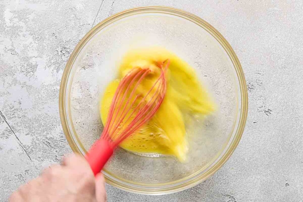 A person whisking eggs in a glass bowl.