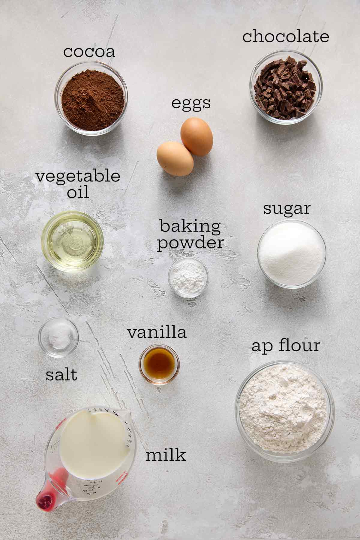 Ingredients for chocolate muffins--cocoa, chocolate, eggs, oil, baking powder, sugar, flour, vanilla, salt, and milk.