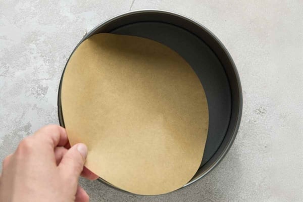 A person's hand sliding a circle of parchment into a cake pan.