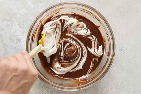 A person folding egg whites into a chocolate batter.