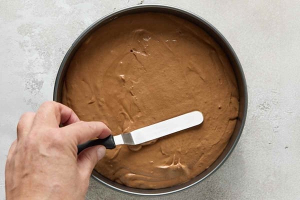 A person's hand smoothing the top of cake batter in a cake pan.