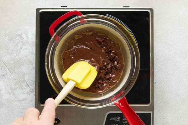A person stirring melted chocolate over a bain marie.