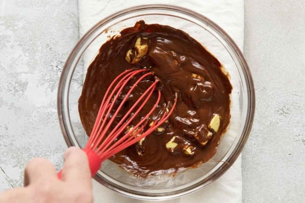 A hand whisking in butter into melted chocolate.