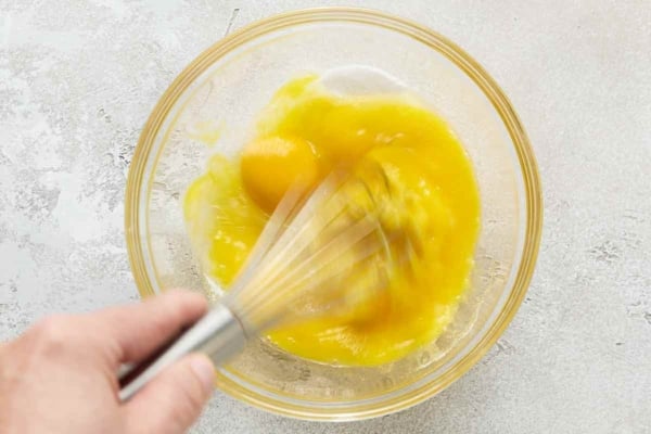 A hand beating egg yolks together.