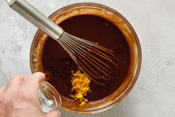 A person's hand pouring Cointreau into melted chocolate.