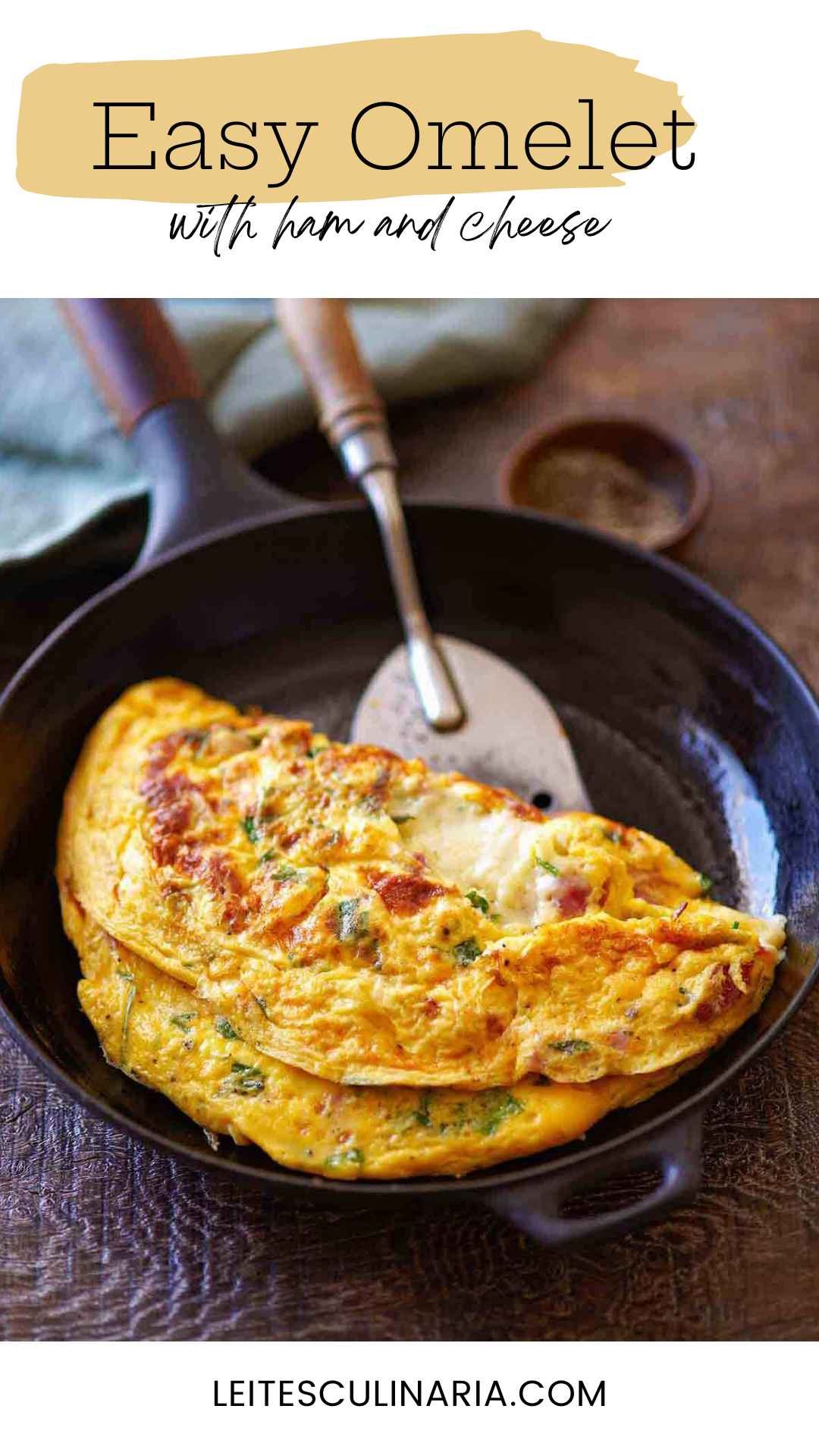 A folded ham and cheese omelet in a skillet with a spatula lifting it.