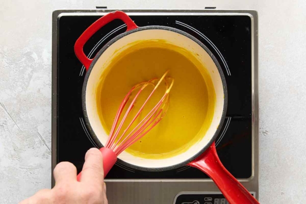 A person whisking homemade mustard in a small pot.