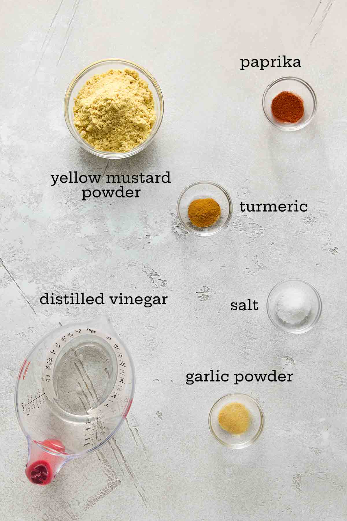 Ingredients for homemade yellow mustard--mustard powder, paprika, turmeric, vinegar, salt, and garlic powder.