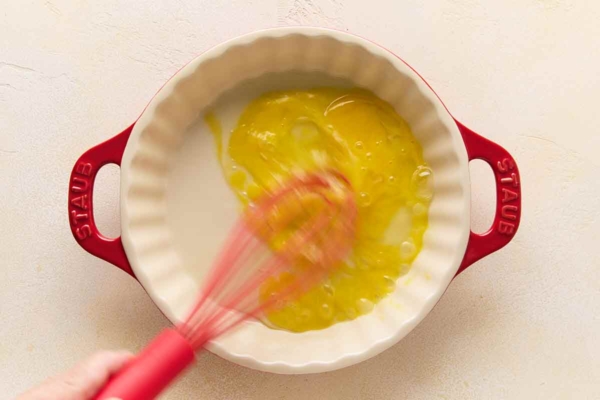 A person's hand whisking egg in a pie plate.