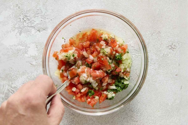 A person mixing salsa ingredients in a small bowl.