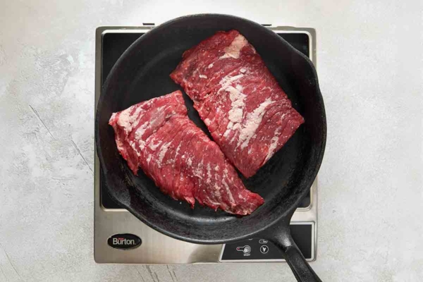 Two pieces of skirt steak in a cast iron pan.