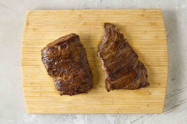Two seared pieces of skirt steak on a cutting board.