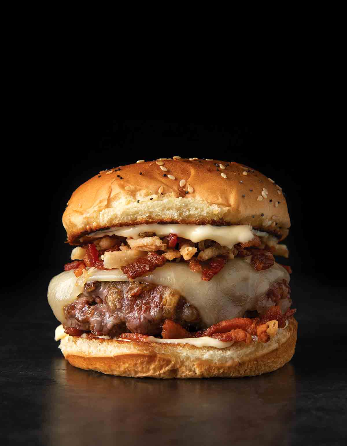 A cheeseburger topped with bacon and crispy onions on a sesame seed bun.