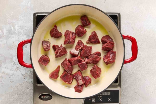 Cubes of beef browning in a cast iron skillet.