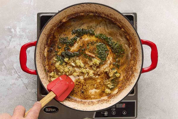 A person stirring garlic and herbs into a butter sauce.