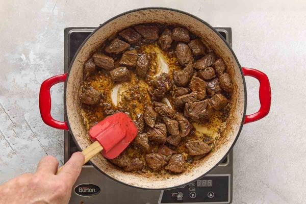 A person stirring browned steak bites into a garlic butter sauce.