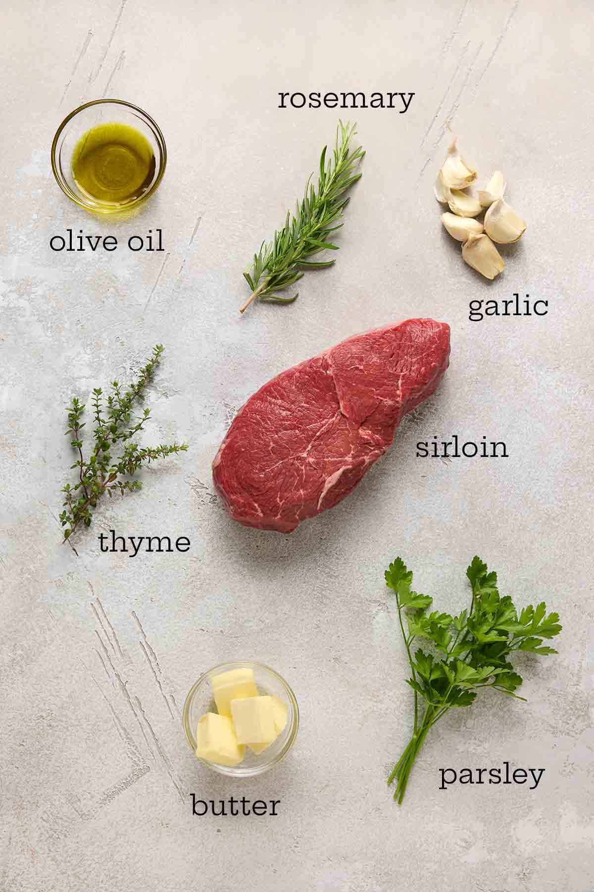 Ingredients for garlic butter steak bites--olive oil, fresh herbs, garlic, butter, and sirloin steak.