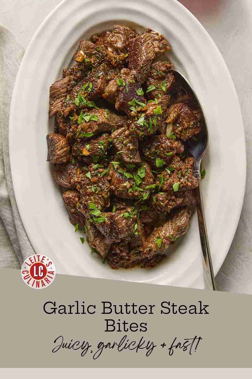 Seared steak cubes garnished with parsley on a white oval platter next to a glass of red wine.