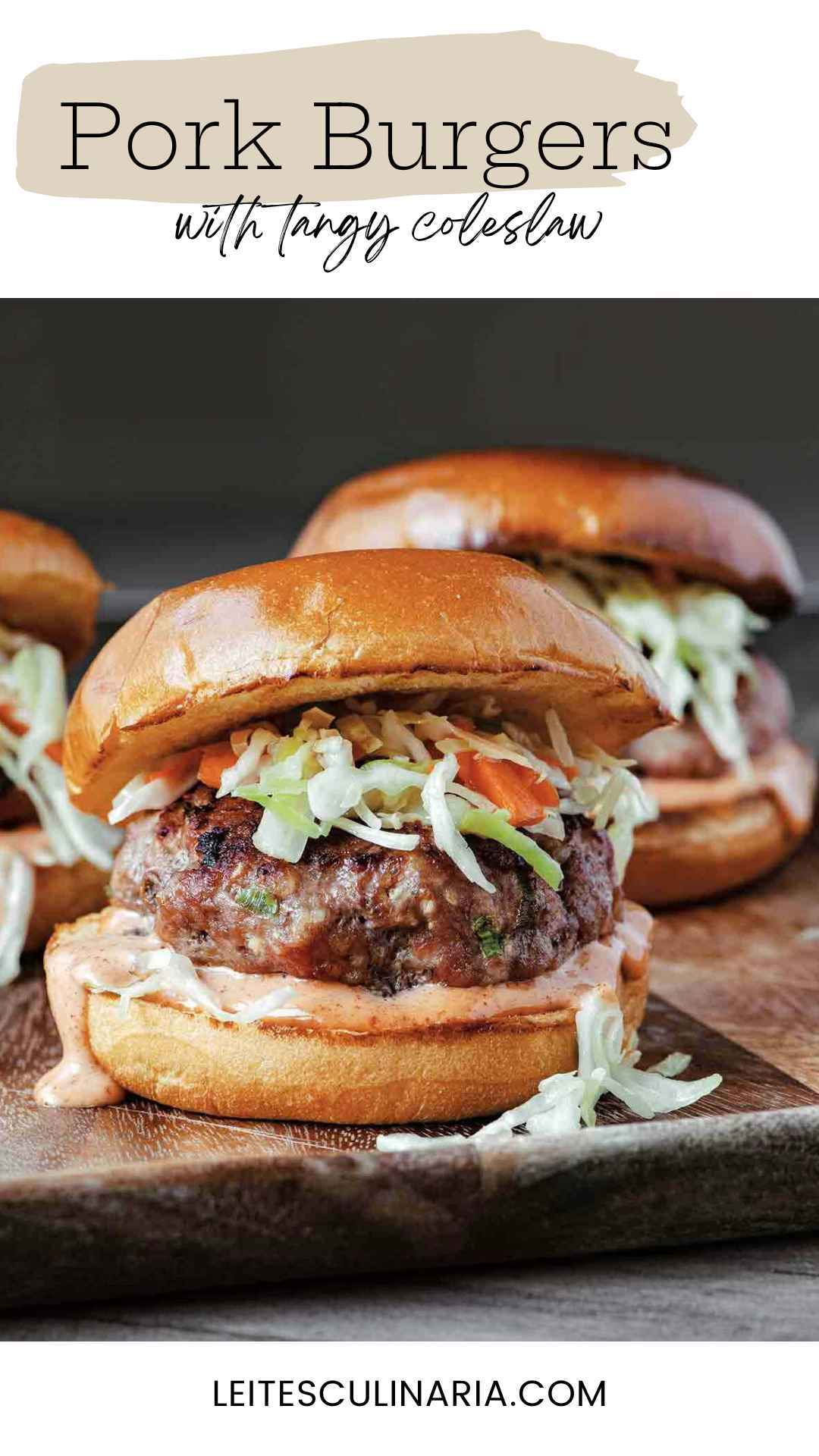 Three grilled pork burgers topped with slaw on toasted buns.