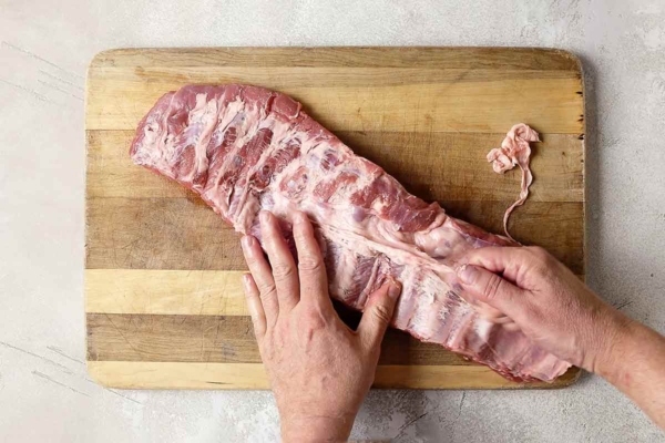 A person removing the membrane from a rack of ribs.