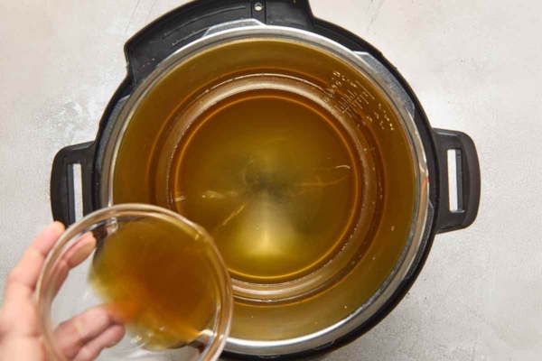 A person pouring broth into a pressure cooker.