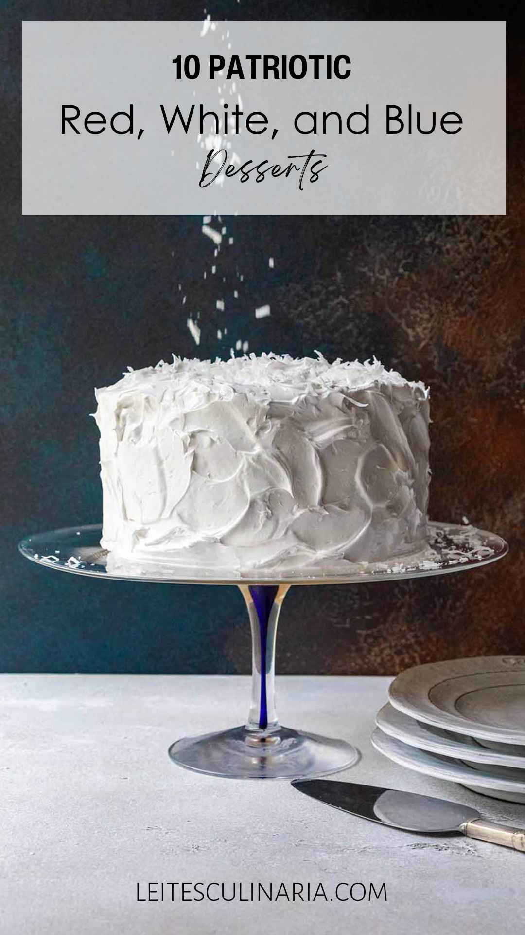 A cake covered in white frosting with coconut flakes falling onto it.