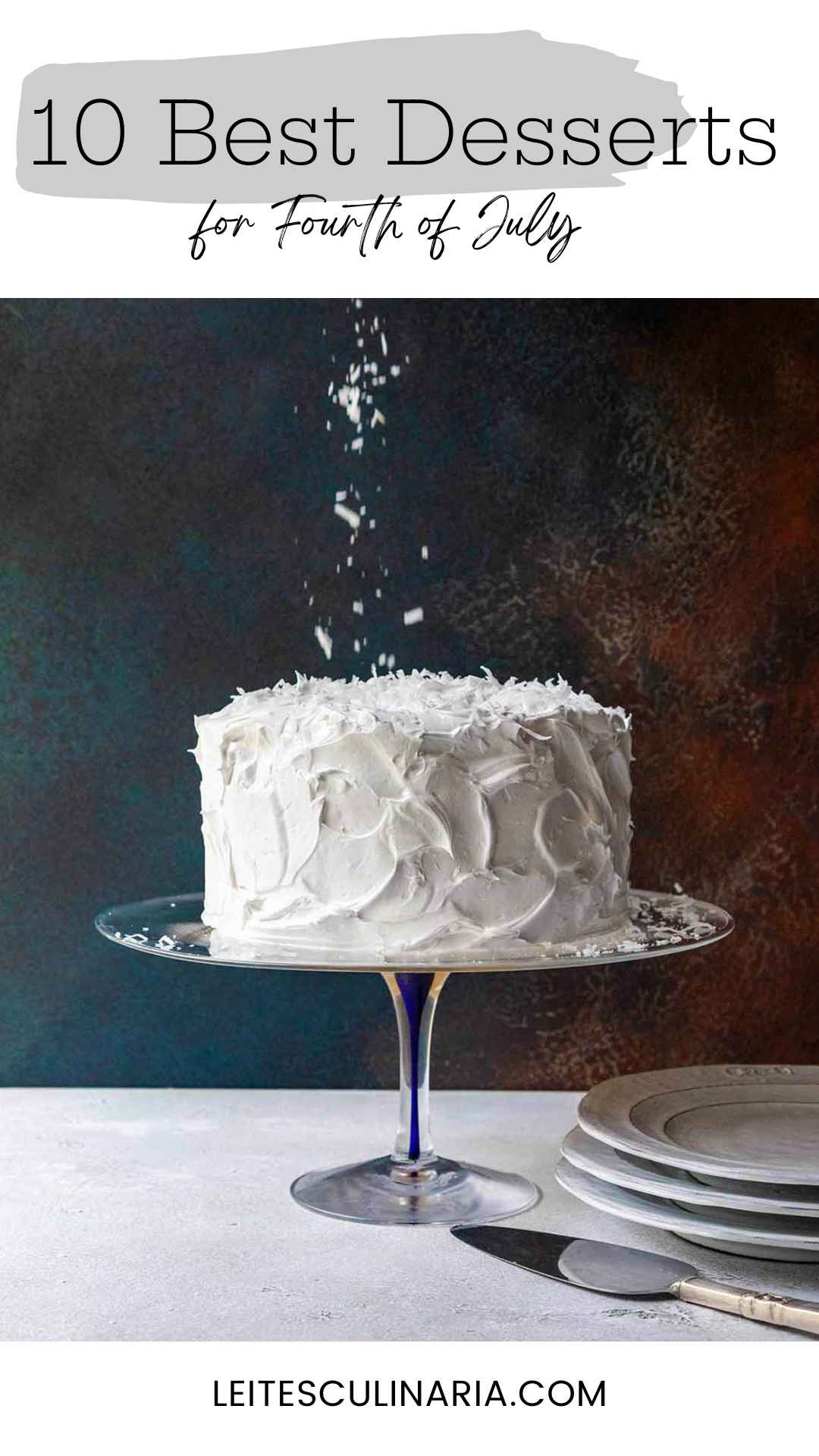A cake covered in white frosting with coconut flakes falling onto it.