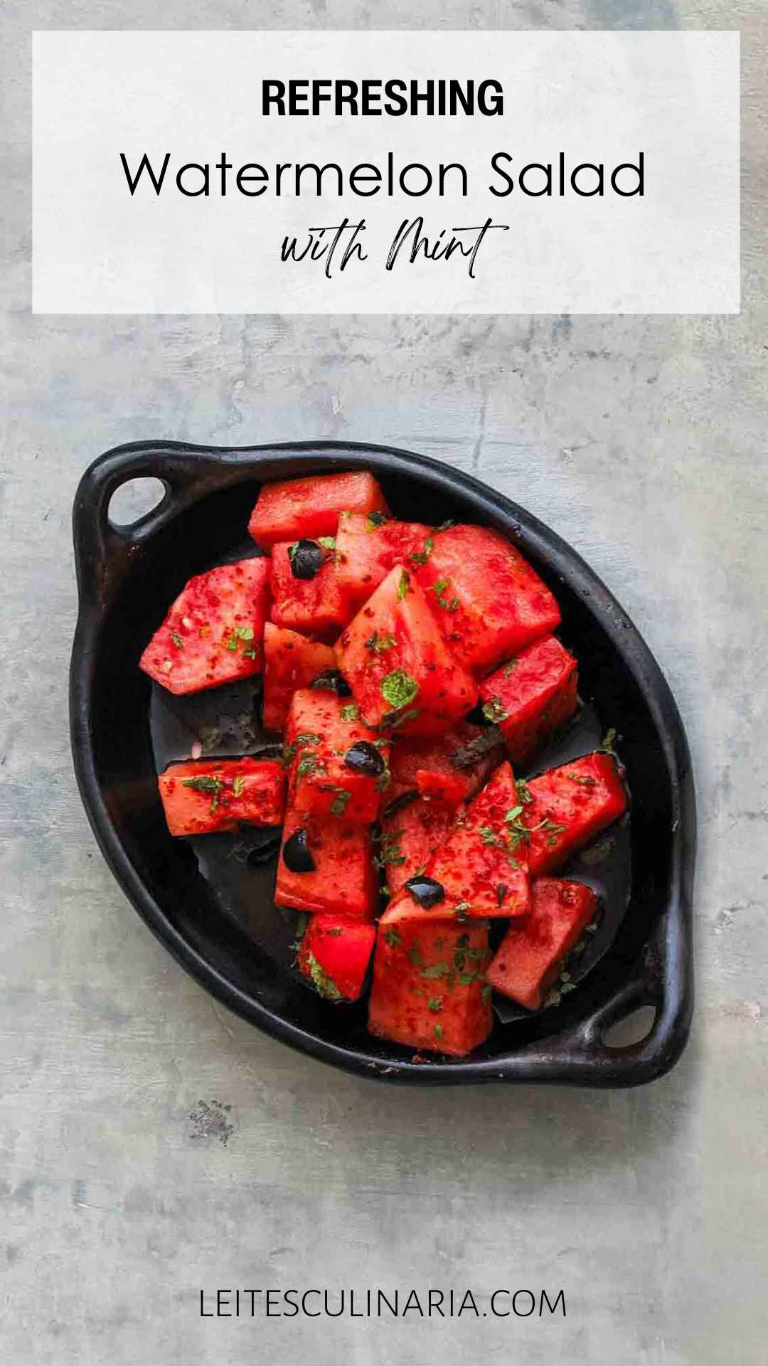 A black dish filled with cubes of fresh watermelon, chopped black olives, and fresh mint leaves.