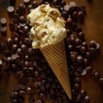 A sugar cone of chocolate chip cookie dough ice cream lying on a bed of chocolate chips.