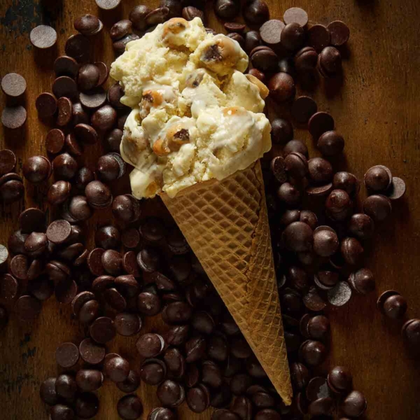 A sugar cone of chocolate chip cookie dough ice cream lying on a bed of chocolate chips.