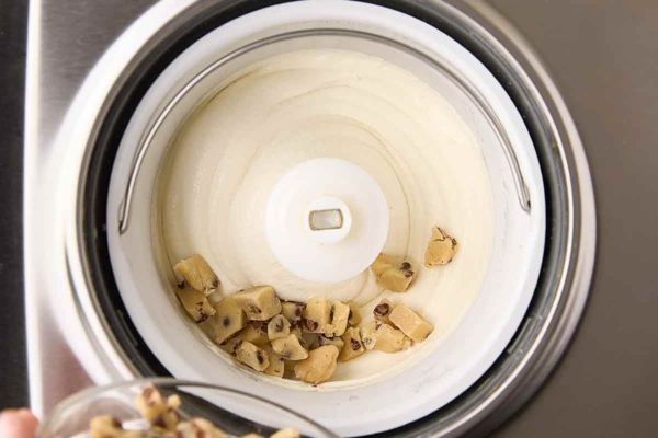 Pieces of chocolate chip cookie dough being added to an ice cream maker.