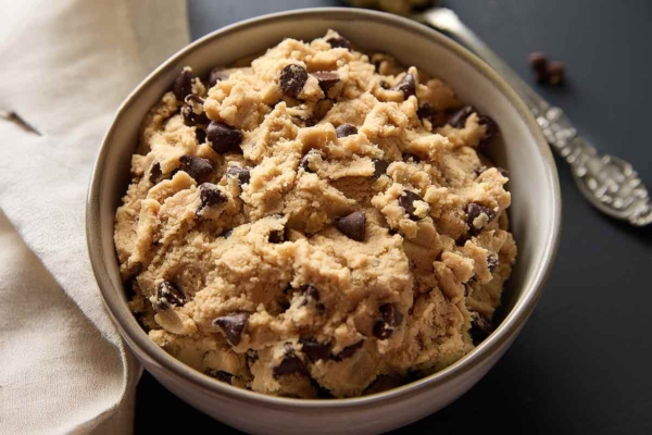 A bowl of edible chocolate chip cookie dough with a spoon and napkin on the side.