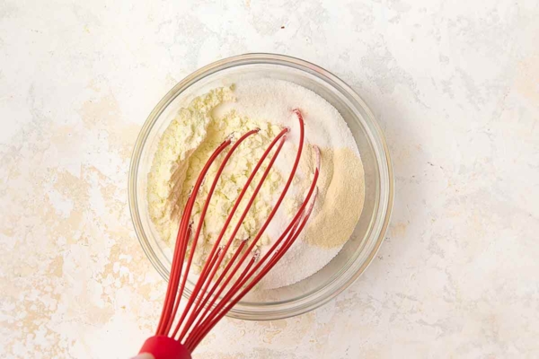 Dry milk powder, sugar, and xanthan gum being whisked together in a bowl.