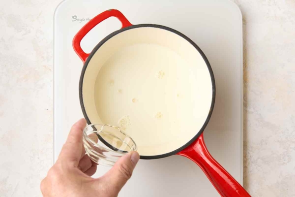 A man's hand drizzling corn syrup into a saucepan of milk.