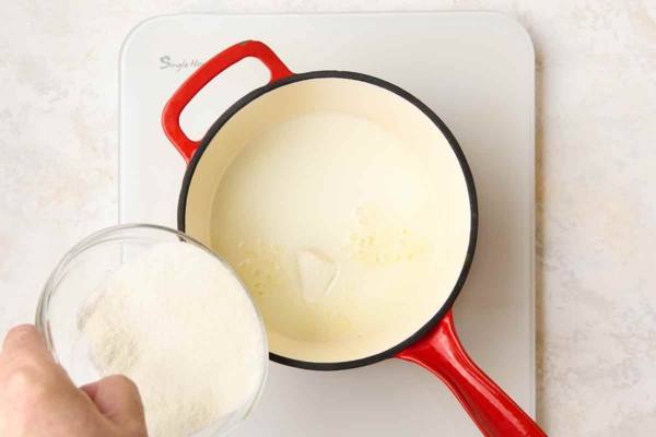 A sugar, xanthan gum, dry milk, and salt mixture being added to a saucepan of milk.