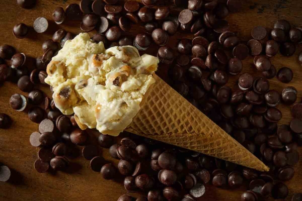 A sugar cone of chocolate chip cookie dough ice cream lying on a bed of chocolate chips.