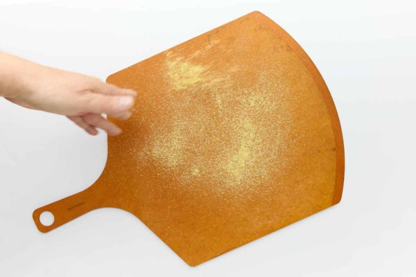 A person dusting a pizza peel with cornmeal.