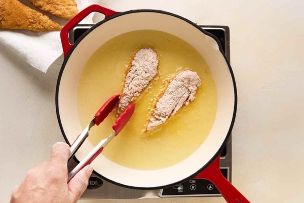 A person frying chicken tenders in a skillet.