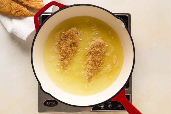 A person frying chicken tenders in a skillet.