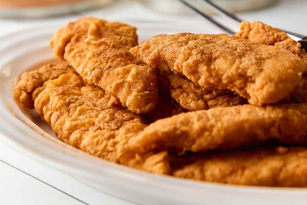 A white oval platter of pan-fried chicken tenders.