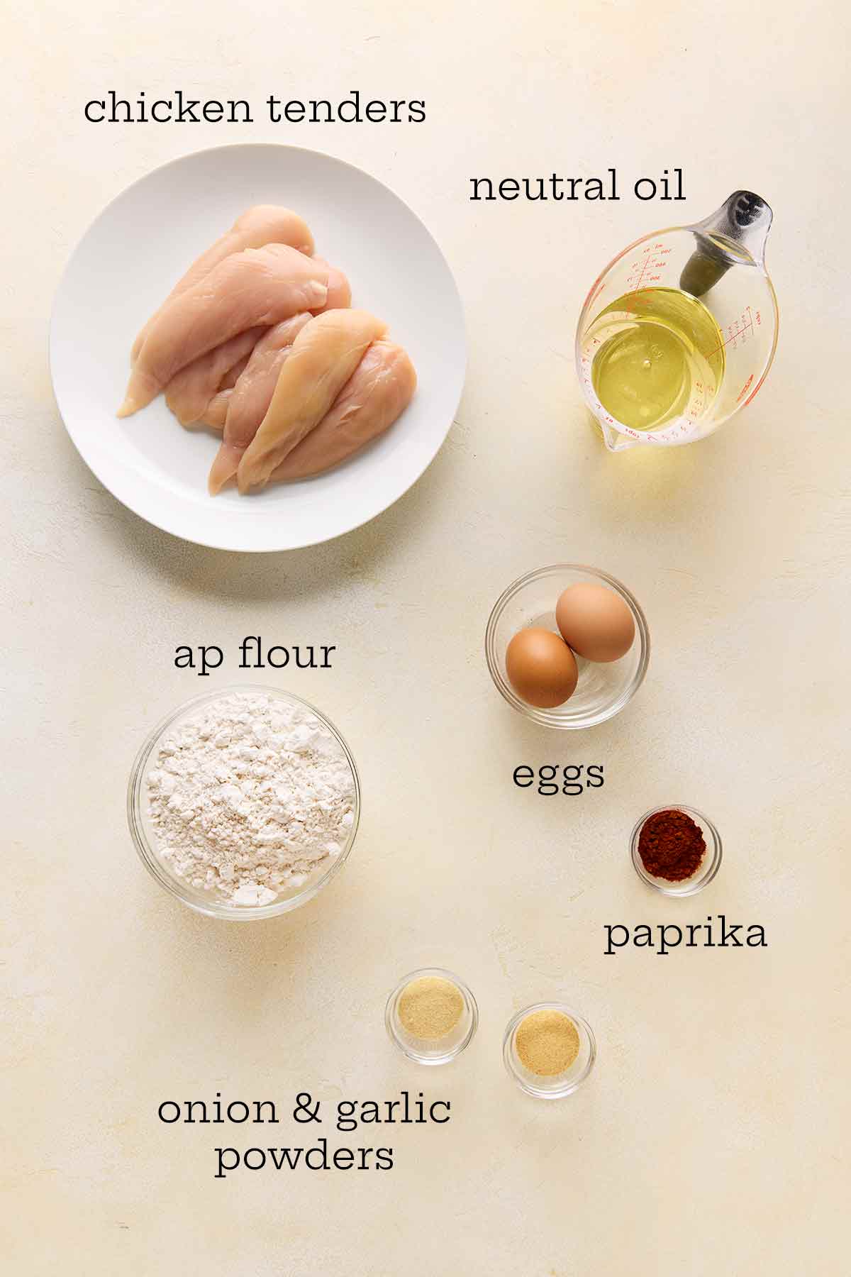 The ingredients for pan-fried chicken tenders: the tenders, oil, flour, eggs, paprika, onion and garlic powders.