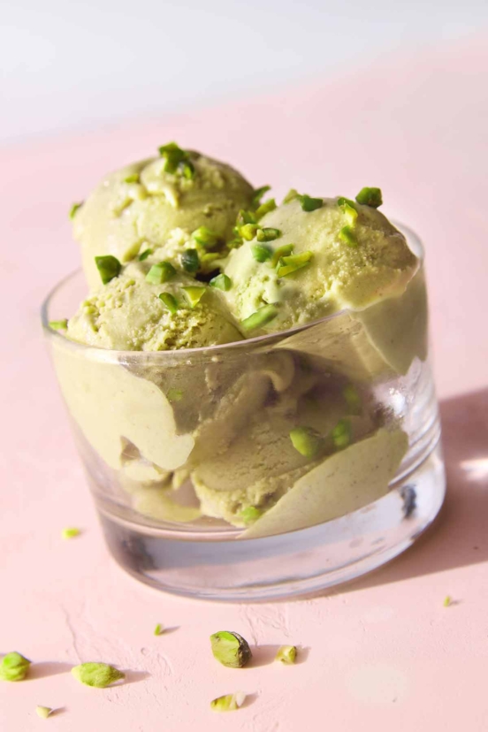 A bowl containing four scoops of pistachio gelato with chopped pistachios on top.