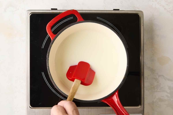 A person stirring cream in a saucepan over a burner.