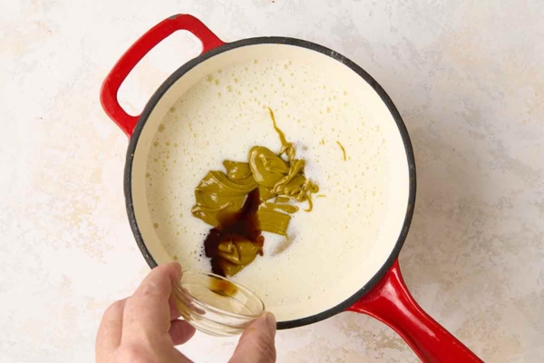 Vanilla and pistachio paste being added to cream in a saucepan.