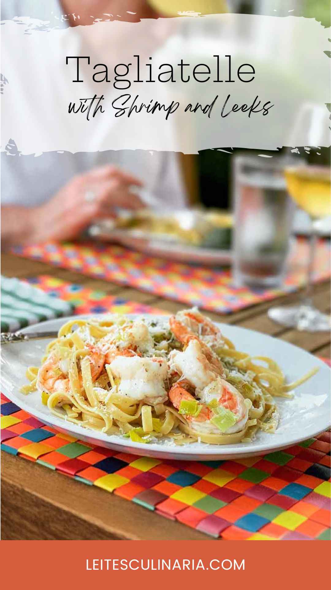 A portion of tagliatelle noodles with shrimp, leeks, and Parmesan on a white plate.