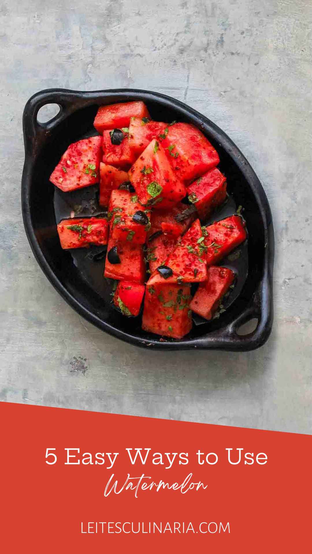A black dish filled with cubed watermelon salad, olives, and mint leaves.